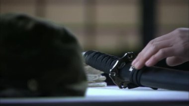 Bir el yavaşça Japon samuray kılıcını masadan kaldırdı.