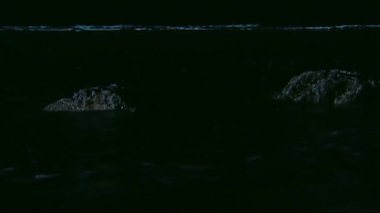 Deniz karanlıkta suda kayalara çarpıyor.