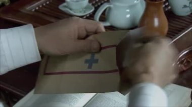 Bir adam zarftan dört haneli Arapça rakam kodlu bir kağıt parçası çıkartıyor, eline yakın plan.