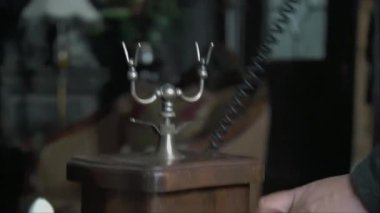 Eski moda bir telefon ahizesini kaldırıp bir adamın elini çevirmeye başlıyorsun.