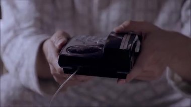 Sabit telefonu iki elinle masaya koy, adamın ellerine yakın çekim yap.