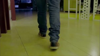 Kot pantolonlu ve günlük ayakkabılı bir adam içeride yürüyor, bacaklarının hareketini kapatıyor.