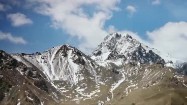 Sabit çekim, beyaz bulutlar mavi gökyüzünün altındaki karlı dağın tepesine hızla sürükleniyor.