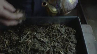 Çaydanlığa çay yaprakları koy ve çaydanlıktan bir kaşık sıcak su getir. Adamın el hareketlerine yakından bakın.