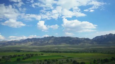 Dağlar, çayırlar ve nehirler yuvarlanan beyaz bulutlar ve mavi gökyüzünün altında