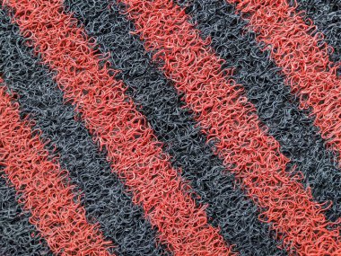 Kıvrımlı plastik döngü desenli kırmızı ve siyah sentetik bir halının yakın çekim makro görüntüsü. Soyut arka planlar, kumaş dokusu veya malzeme yüzey tasarımı için ideal.
