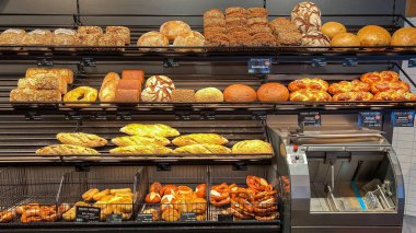 Ekmek, ekmek ve krakerlerin çeşitli çeşitleri düzenli ve davetkar bir şekilde düzenlenmiş bir fırında sergilenmekte olan taze ekmek ve hamur işleri çeşitliliği.