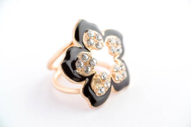 Parlak siyah taç yaprakları ve metalik bir zemine sabitlenmiş parlak parlak taşlardan oluşan çiçek şeklinde bir yüzüğün yakın çekimi. Yumuşak ışıklandırma ve ince detay ile beyaz bir arkaplanda fotoğraflandı.