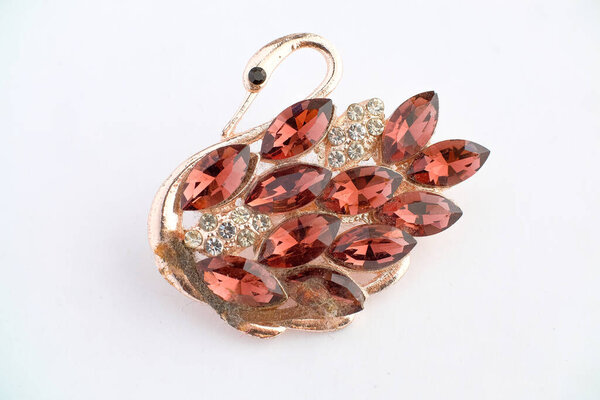 Close-up image of a decorative brooch shaped like a swan, adorned with marquise-cut red gemstones and round clear crystals on a gold-tone base. Photographed on a white background.