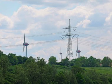 Rüzgar türbini, yüksek voltaj direği. Bir rüzgar türbini ve yüksek voltaj direğinin fotoğrafı sürdürülebilir enerji üretimini ve yenilenebilir enerji kaynaklarına geçişi sembolize eder.