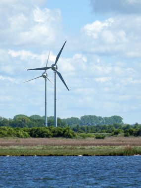 Geniş yeşil bir arazide iki yalnız rüzgar türbini duruyor. Geniş görüş. Uzayı kopyala Metinler ve tasarımlar için boşluk.