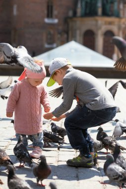 Şehir meydanında güvercinlerle oynayan iki çocuk. Neşeli an