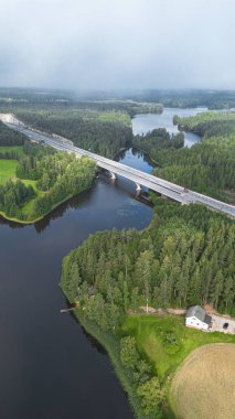 Finlandiya 'da nehir ve orman manzarası boyunca uzanan karayolu köprüsünün havadan görünüşü