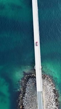 Norveç, Lofoten Adaları 'ndaki beyaz bir köprünün kuş bakışı görüntüsü. Aşağıdaki turkuaz sulardan geçen kırmızı bir araba..