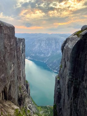 Norveç 'te bulutlu bir gökyüzünün altında çarpıcı bir fiyorda bakan sarp bir uçurum manzarası