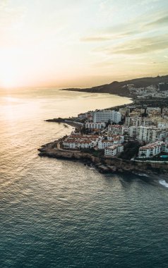 Gün batımında bir sahil kasabasının havadan görünüşü, kıyı şeridi boyunca binalar ve ufukta uzanan deniz..
