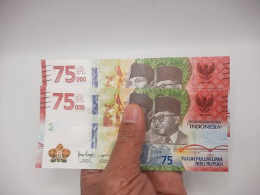 Elinde 75 bin rupi değerinde, beyaz bir arka planı olan Endonezya banknotu. 