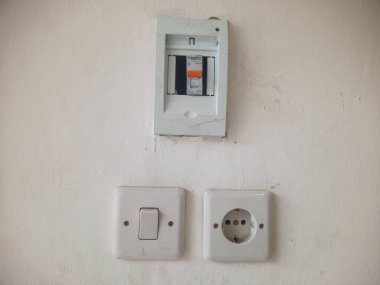 Üç bileşenden oluşan beyaz bir duvara monte edilmiş basit bir elektrik kurulumunu gösterir: MCB, ışık anahtarı ve soket. 