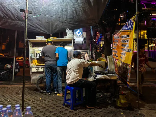 Bandung, Endonezya - 15 Haziran 2025 'te kalabalık bir sokak yiyecek standında birkaç adamın çadırın altında yemek hazırlayıp sattığı bir akşam manzarası
