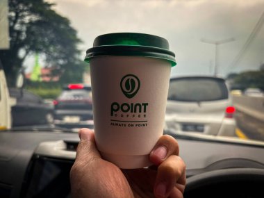 tangerang, indonesia - june 21, 2025 : Hand holding a cup of Point Coffee in a car with a highway background 