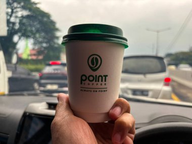 tangerang, indonesia - june 21, 2025 : Hand holding a cup of Point Coffee in a car with a highway background 
