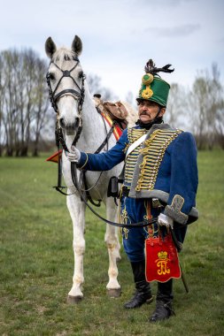 Yeşil bir arazide beyaz bir atın üzerinde bir Macar süvarisi. 1848-49 Devrim ve Bağımsızlık Savaşı elbisesi. Tapiobicske - Macaristan 04.04.2023.