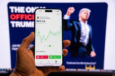 Elinde Moonshot uygulamasında resmi Trump mim logosunu gösteren bir telefon tutan adam, satın alınmaya hazır, arka planda mim 'in grafiğini gösteren bulanık bir monitör var. Budapeşte, Macaristan - 20 Ocak 2025