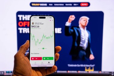 Elinde Moonshot uygulamasında resmi Trump mim logosunu gösteren bir telefon tutan adam, satın alınmaya hazır, arka planda mim 'in grafiğini gösteren bulanık bir monitör var. Budapeşte, Macaristan - 20 Ocak 2025