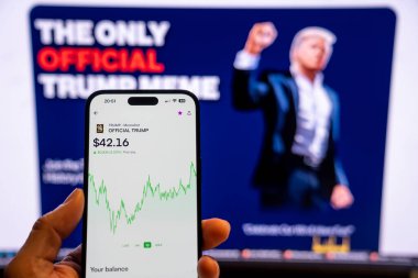 Elinde Moonshot uygulamasında resmi Trump mim logosunu gösteren bir telefon tutan adam, satın alınmaya hazır, arka planda mim 'in grafiğini gösteren bulanık bir monitör var. Budapeşte, Macaristan - 20 Ocak 2025