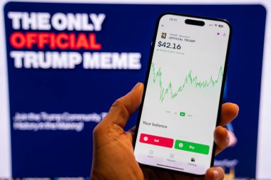 Elinde Moonshot uygulamasında resmi Trump mim logosunu gösteren bir telefon tutan adam, satın alınmaya hazır, arka planda mim 'in grafiğini gösteren bulanık bir monitör var. Budapeşte, Macaristan - 20 Ocak 2025