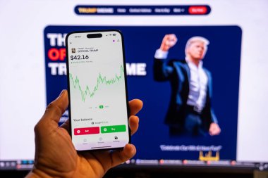 Elinde Moonshot uygulamasında resmi Trump mim logosunu gösteren bir telefon tutan adam, satın alınmaya hazır, arka planda mim 'in grafiğini gösteren bulanık bir monitör var. Budapeşte, Macaristan - 20 Ocak 2025
