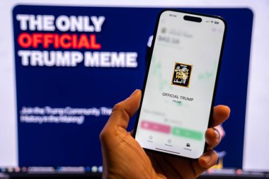 Elinde Moonshot uygulamasında resmi Trump mim logosunu gösteren bir telefon tutan adam, satın alınmaya hazır, arka planda mim 'in grafiğini gösteren bulanık bir monitör var. Budapeşte, Macaristan - 20 Ocak 2025