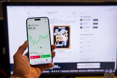 Elinde Moonshot uygulamasında resmi Trump mim logosunu gösteren bir telefon tutan adam, satın alınmaya hazır, arka planda mim 'in grafiğini gösteren bulanık bir monitör var. Budapeşte, Macaristan - 20 Ocak 2025