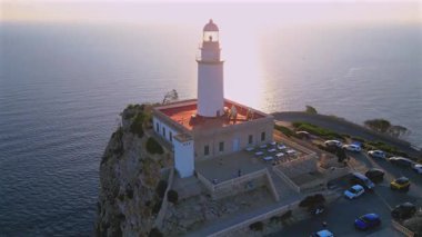 Far de Formentor, 4K Aerial Drone 'un geniş deniz ufkundan kayalıkların kenarındaki pitoresk deniz fenerinin üzerinden alevli kırmızı gündoğumu videosu. Pollenca, Mallorca, İspanya. İHA hareketlerini geri çek.