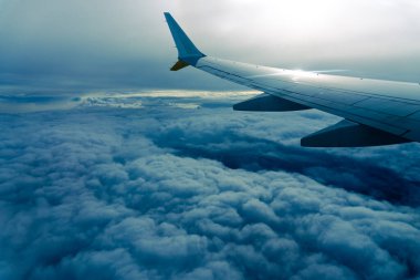 Bulutların üstünde uçak kanadı. Bir uçak penceresinden (pencere) görüntüsü. İspanya 'nın Balear Adası' nda mavi gökyüzünde yansıyan güneş ışığı.