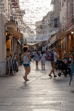Alcudia, Mallorca, İspanya. Geleneksel binaları, dükkanları ve restoranları olan antik bir kasabada çok işlek bir caddenin manzarası. Süslemeler caddeye gölge düşürüyor.