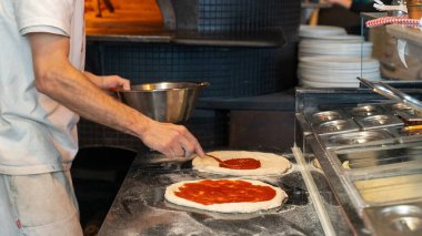 Yakın plan. Önlüklü erkek fırıncı mutfak masasında taze pizza pişiriyor.