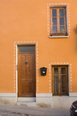 Ahşap kapılı ve pencereli parlak turuncu bina cephesi. Mimari detaylar, canlı bir renk ve bir yer duygusu..