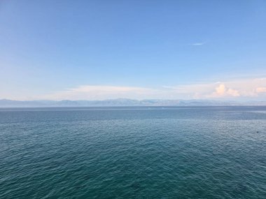 Ufuk açık mavi gökyüzüne karışan uzak dağlarla birlikte. Geniş deniz manzarası ve sakin atmosfer.