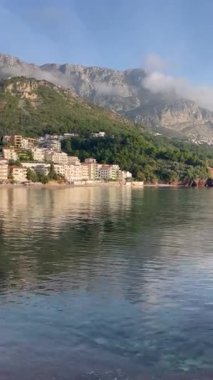 Karadağ 'ın Sveti Stefan kentindeki dağlar ve plajlar. Deniz, kum, beyaz evler ve bulutlardaki dağlar güneşli bir günde