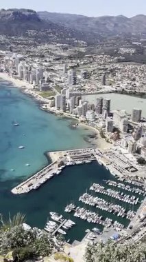 Calpe kıyılarının panoramik manzarası, Costa Blanca, Alicante bölgesi, İspanya. Kumsal boyunca gökdelenler, mavi Balear Denizi ve güneşli sıcak bir günde dağlar. İspanya 'da bir tatil köyünde tatil. Dikey video.