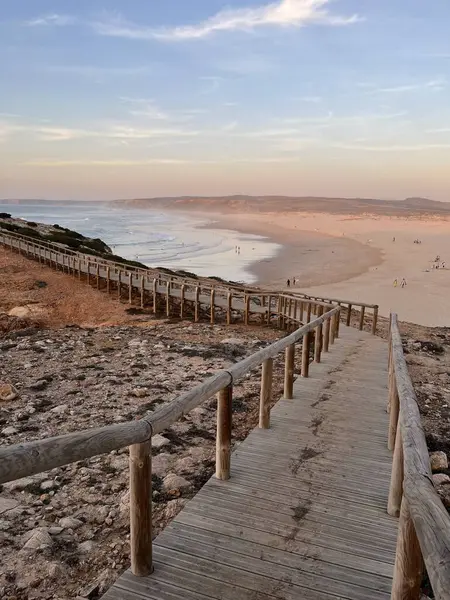Tahta bir patika, günbatımında aydınlatılan Atlantik kıyısındaki kumlu bir sahile çıkıyor. Praia da Bordeira, Carrapateira, Portekiz.