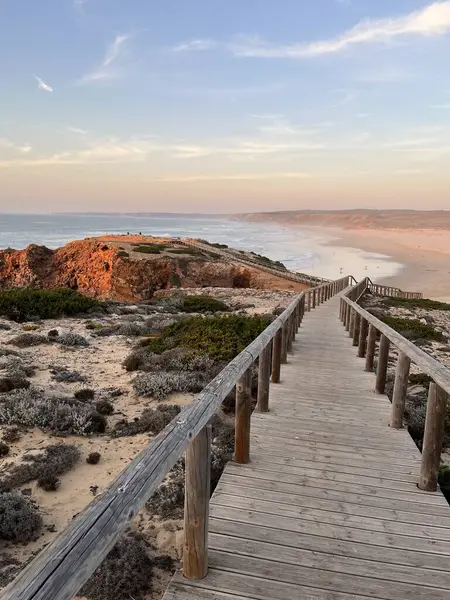 Tahta bir patika, günbatımında aydınlatılan Atlantik kıyısındaki kumlu bir sahile çıkıyor. Praia da Bordeira, Carrapateira, Portekiz.