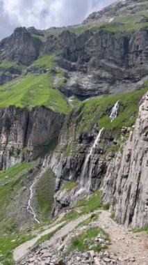 Şelaleler yazın İsviçre Alpleri 'ndeki yeşil çimenler arasında kayalık uçurumların üzerinden akar, Oeschinensee Gölü, Kandersteg