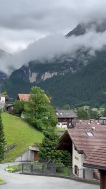 Alp dağlarındaki yeşil çayırlar ve ormanların arasındaki ahşap evlerin olduğu köye giden bir trenden alçak bulutların altındaki Grindelwald, İsviçre