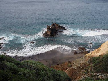 Benijo sahilinde mavi suyu ve Atlantik okyanusu dalgaları olan alışılmadık şekilli siyah bir kaya. Tenerife 'nin volkanik manzarası, Kanarya Adaları, İspanya.
