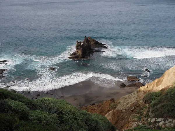 Benijo sahilinde mavi suyu ve Atlantik okyanusu dalgaları olan alışılmadık şekilli siyah bir kaya. Tenerife 'nin volkanik manzarası, Kanarya Adaları, İspanya.