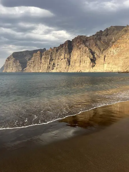 Günbatımında Los Gigantes uçurumları güneş, siyah kum plajı ve mavi Atlantik Okyanusu 'nun sakin dalgaları tarafından aydınlatılır. Tenerife, Kanarya Adaları, İspanya.