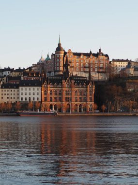 İsveç 'in Stockholm kentinden, Sodermalm bölgesinin tarihi manzarası, gün batımının altın saatinde. Mariaberget Riddarfjarden suyuna yansıyor. İskandinav mimarisi.