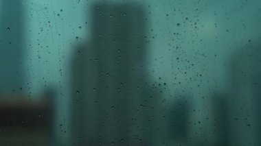 Yağmurlu bir günü gösteren bulanık arkaplanlı pencereye yağmur damlaları